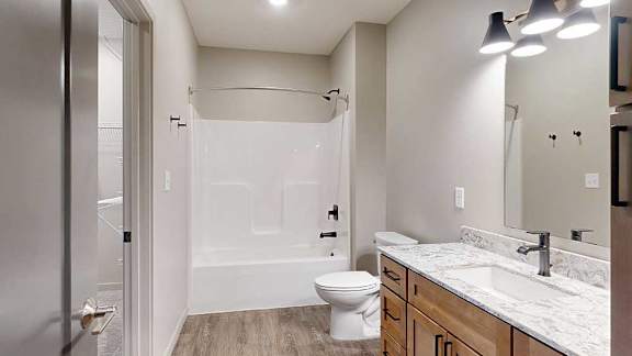A bathroom with a quartz vanity, warm wooden cabinets, and a tub shower with black fixtures.
