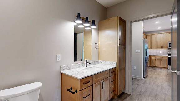 A walk-through bathroom with a wide quartz vanity and a door open to the front entryway.