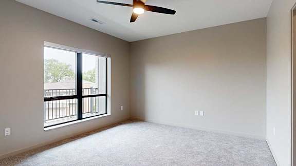 A carpeted bedroom with a ceiling fan and a floor-to-ceiling window.