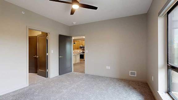A carpeted bedroom with a walk-in closet, attached bathroom, and a door open to the living room.