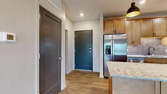 A front entryway next to a modern kitchen with warm wooden cabinets and stainless steel appliances.