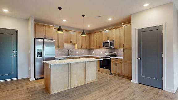 A kitchen with warm wooden cabinets, quartz countertops, an island, and stainless steel appliances.