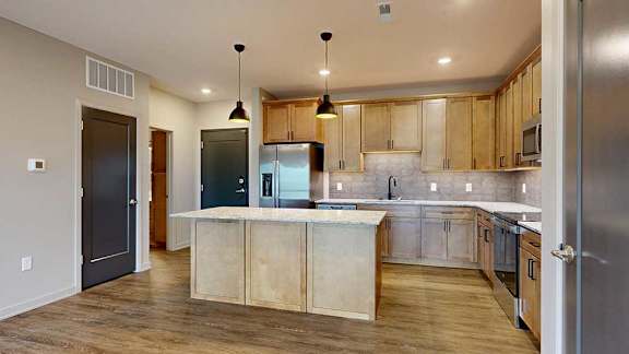 A kitchen with warm wooden cabinets, quartz countertops, an island, and stainless steel appliances.