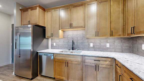 A modern kitchen sink with quartz counters, warm wooden cabinets, and a tile backsplash.