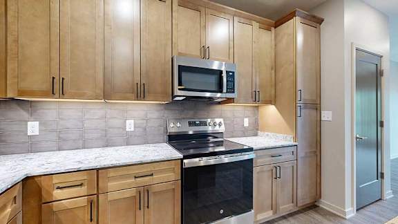 A close up of the stainless steel microwave and range in a kitchen with warm wooden cabinets.