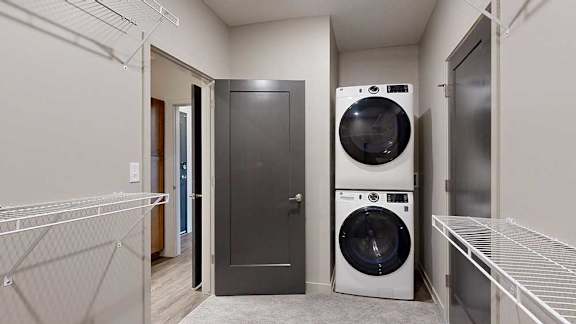 A walk-through closet with wire shelving on either side, a stacked washer and dryer, and a door open to an attached bathroom.