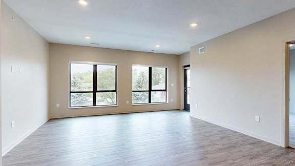 A living room with hardwood-style flooring and floor-to-ceiling windows.