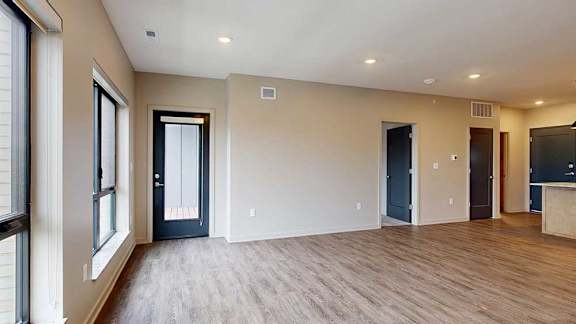 A living room with hardwood-style flooring, floor-to-ceiling windows, and a windowed door to a balcony.