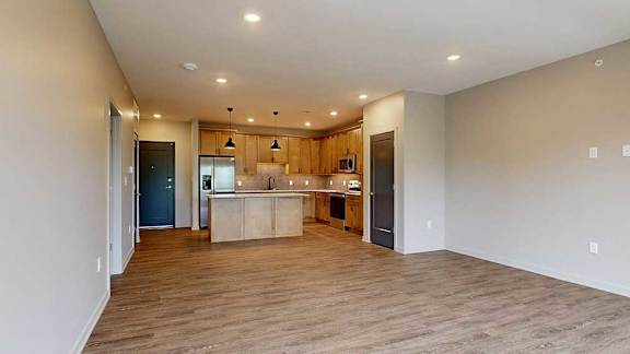 A living room with hardwood-style flooring and kitchen with warm wooden cabinets.