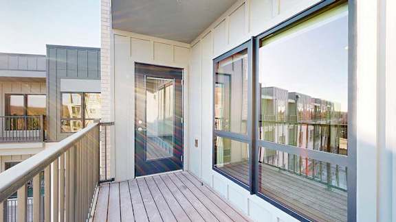 A balcony with a metal railing, a windowed door to the living room, and a view of the courtyard.