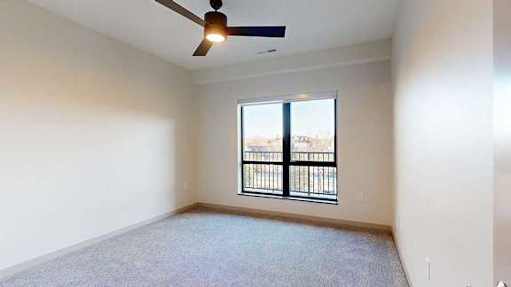 A bedroom with a large floor-to-ceiling window, a ceiling fan, and carpeted flooring.