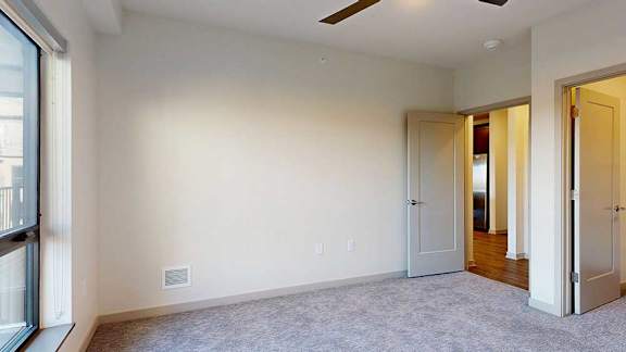 A bedroom with floor-to-ceiling windows, a ceiling fan, and a walk-in closet.