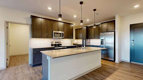 A kitchen with dark wooden cabinets, quartz countertops, an island, and stainless steel appliances.