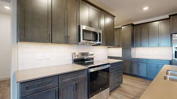 A close up of the stainless steel microwave and range in a kitchen with dark wooden cabinets.