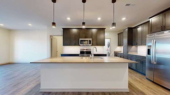 A kitchen with dark wooden cabinets, quartz countertops, an island, and stainless steel appliances.