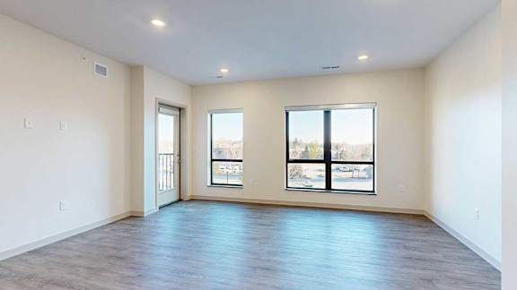 A living room with hardwood-style flooring and floor-to-ceiling windows.