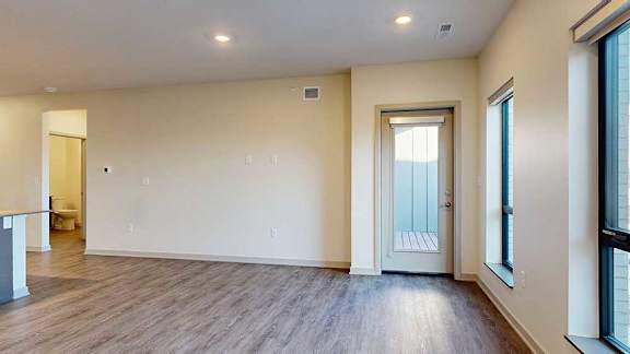 A living room with hardwood-style flooring, floor-to-ceiling windows, and a windowed door to a balcony.