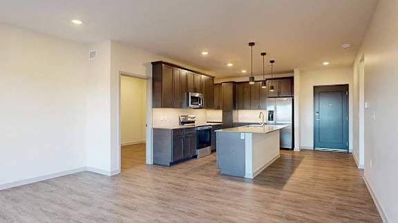 A living room with hardwood-style flooring and kitchen with dark wooden cabinets.