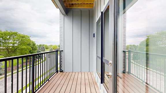 Private apartment balcony with wood decking, black metal railing, and treetop views.