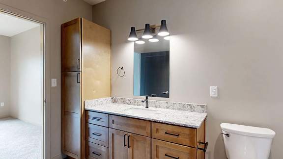 Modern apartment bathroom with a single-sink vanity, wood cabinetry, and a large mirror.