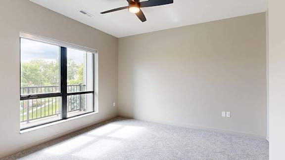A room with a ceiling fan and a large window overlooking a balcony.