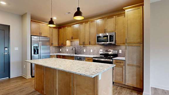 Modern apartment kitchen with a large island, wood cabinetry, and stainless steel appliances.