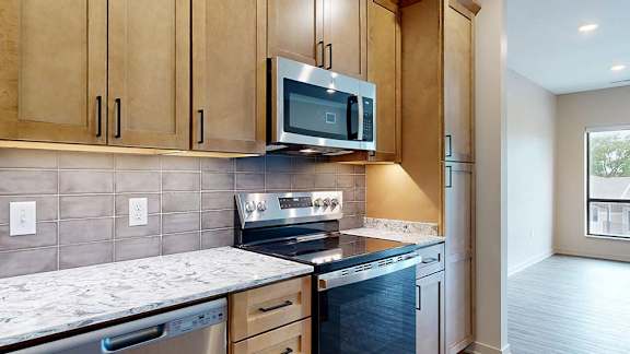Modern apartment kitchen with wood cabinetry, stainless steel appliances, and a tile backsplash.