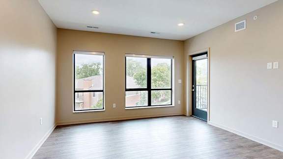 Bright apartment living area with wood-style flooring, large windows, and a door leading to a private balcony.