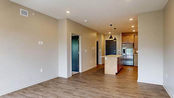 Open-concept apartment living area with wood-style flooring and a kitchen with an island.