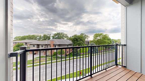 Private apartment balcony with black metal railing and views of neighboring homes and trees.