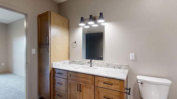 Modern apartment bathroom with a single-sink vanity, wood cabinetry, and a large mirror.