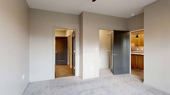 Bright apartment bedroom with carpeted flooring and open doorways to the hallway and bathroom.