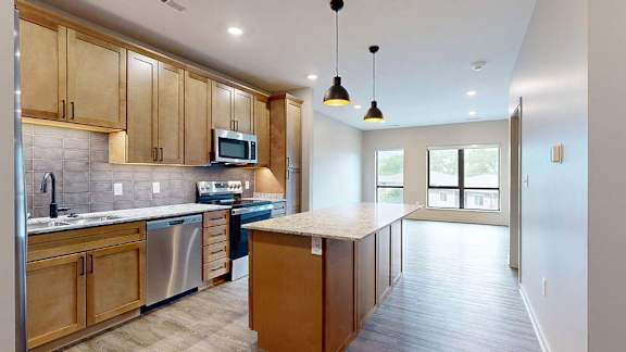 Modern apartment kitchen with a large island, wood cabinetry, and stainless steel appliances.
