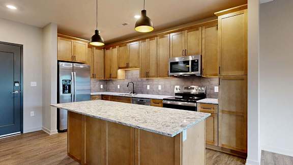 Modern apartment kitchen with a large island, wood cabinetry, and stainless steel appliances.