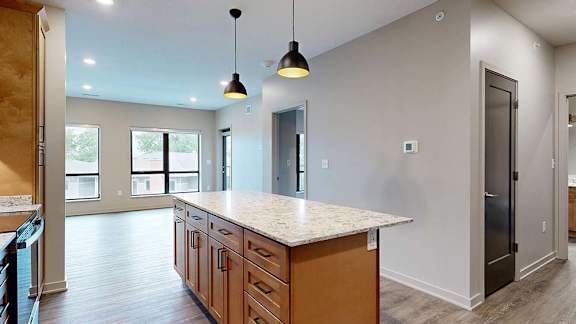 Bright apartment kitchen with a waterfall-style island, pendant lighting, ample cabinet storage, and an open view into the living room.