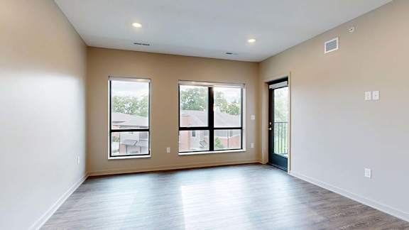 Bright apartment living area with wood-style flooring, large windows, and a private balcony.