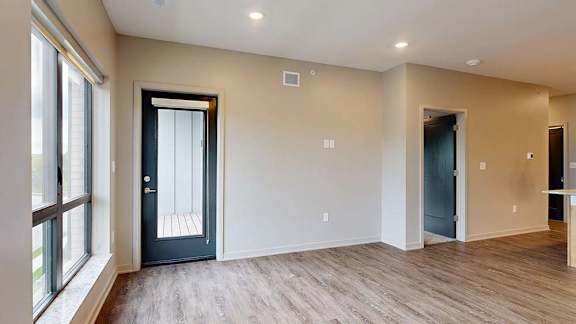 Bright apartment living area with wood-style flooring, large windows, and a door leading to a private balcony.