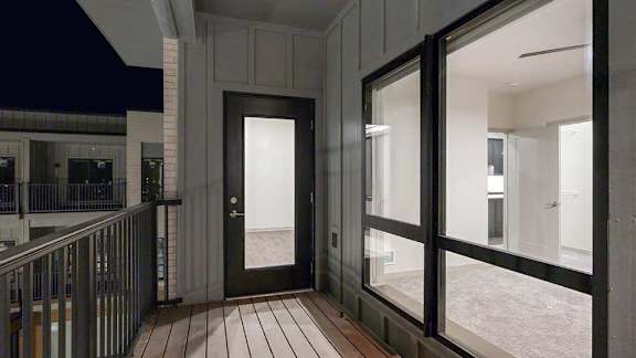 Private apartment balcony with wood-look decking, metal railing, and a glass door and window connecting to the interior.