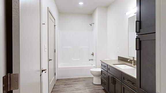Apartment bathroom with dark cabinetry, a light countertop, wood-look flooring, and a bathtub and shower combination.