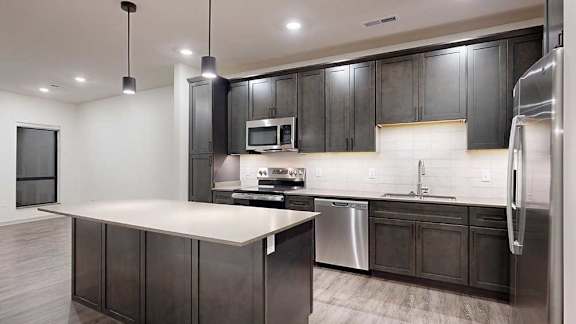 Modern apartment kitchen with dark cabinetry, stainless steel appliances, a large island, and pendant lighting.