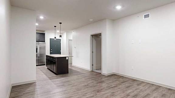 Open-concept apartment interior with wood-look flooring, recessed lighting, and a kitchen island with pendant lights.