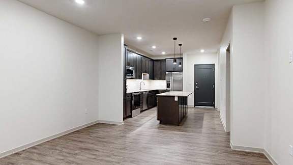 Open-concept apartment living area with wood-look flooring, recessed lighting, and a kitchen with a center island.