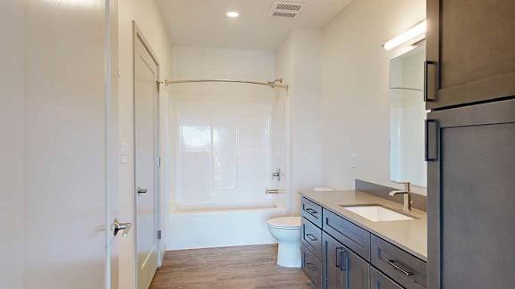 A bathroom with a quartz vanity, dark wooden cabinets, and a tub shower with brushed nickel fixtures.