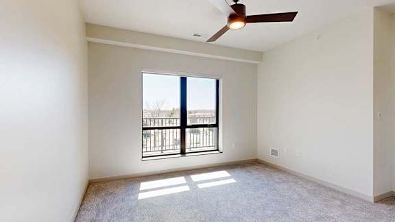 A bedroom with a large floor-to-ceiling window, a ceiling fan, and carpeted flooring.