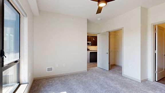 A bedroom with floor-to-ceiling windows, a ceiling fan, an ensuite bathroom, and walk-in closet.
