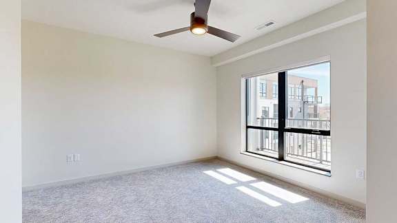 A carpeted bedroom with a ceiling fan and a floor-to-ceiling window.