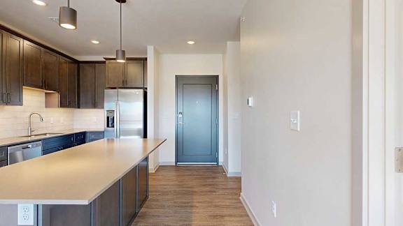 A front entryway next to a modern kitchen with dark cabinets and stainless steel appliances.