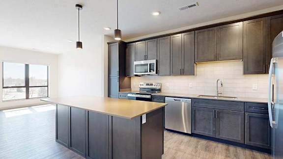 A kitchen with dark wooden cabinets, quartz countertops, an island, and stainless steel appliances.