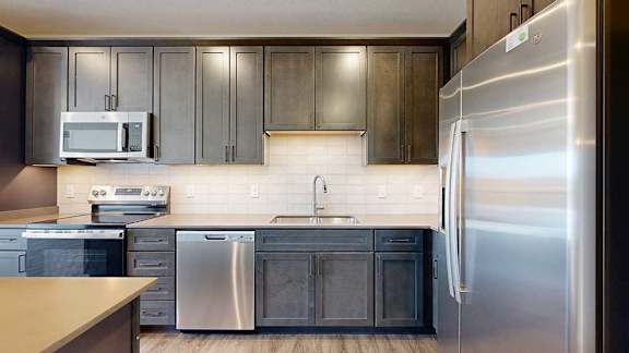 A modern kitchen sink with quartz counters, dark wooden cabinets, and a tile backsplash.