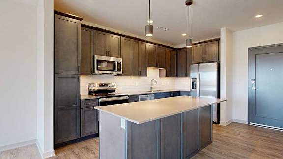 A kitchen with dark wooden cabinets, quartz countertops, an island, and stainless steel appliances.
